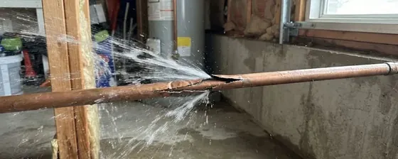 Burst copper pipe spraying water inside a basement near a water heater