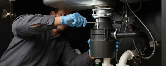 Technician working on a garbage disposal under a kitchen sink