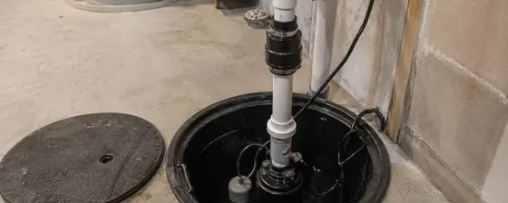 Sump pit with a pump and white discharge pipe in a basement floor