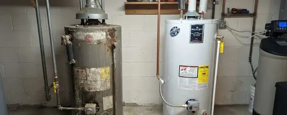 Old rusted tank water heater standing beside a new replacement unit in a basement